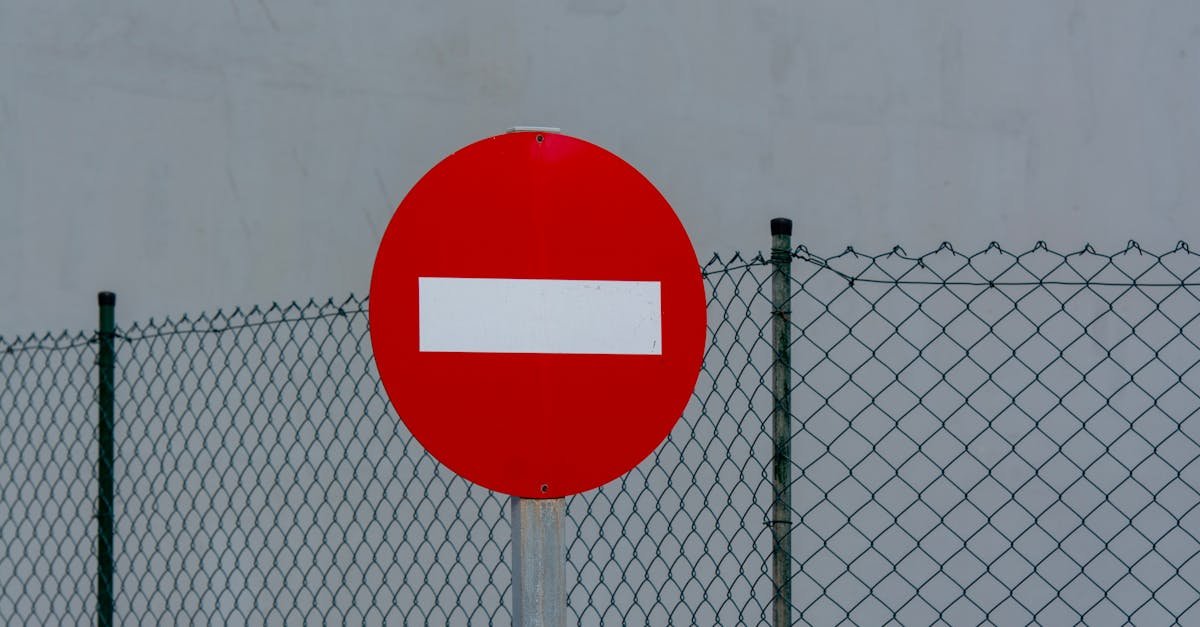 Red circular no entry sign in front of a mesh fence, symbolizing prohibition and security.